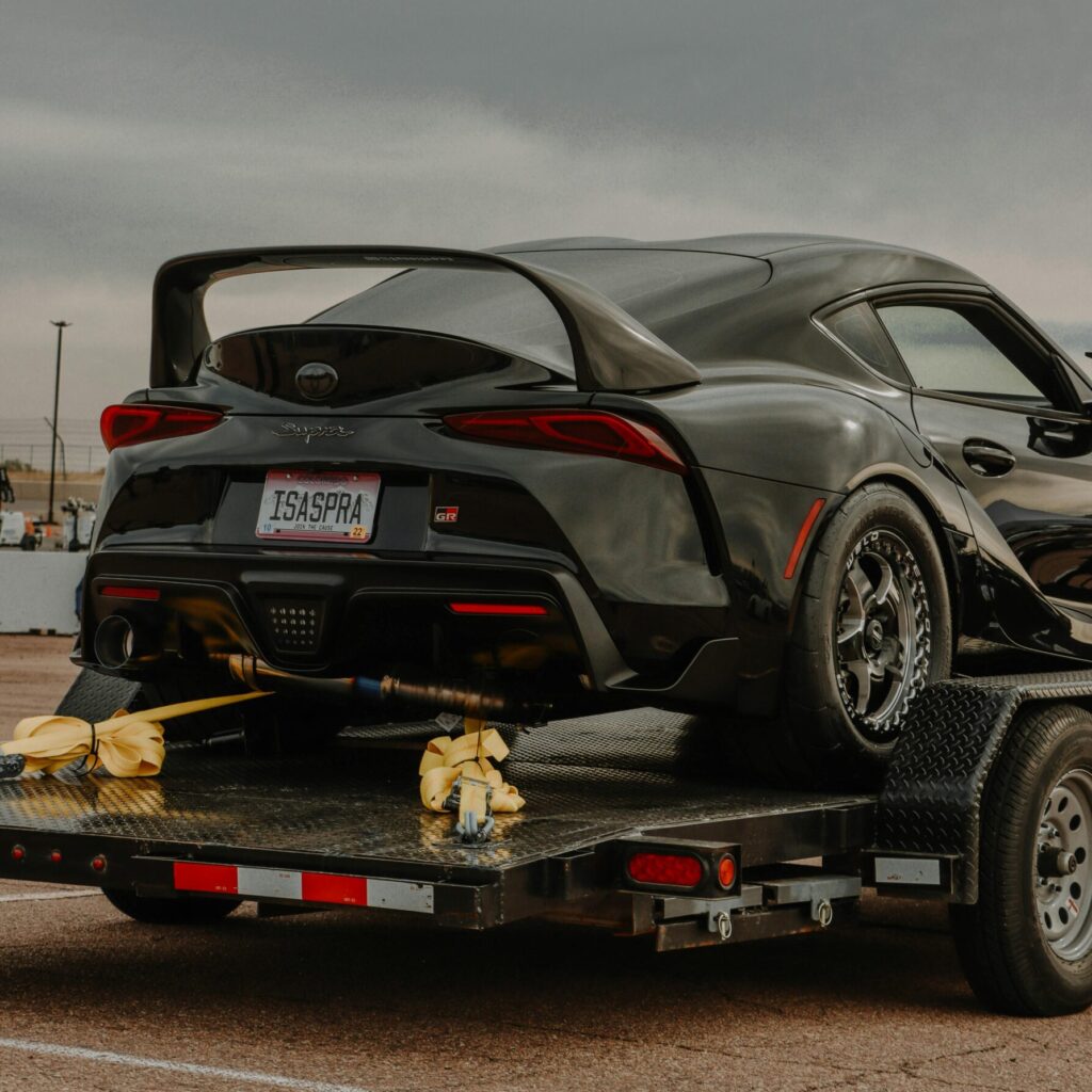 A sleek black sports car with a spoiler on a trailer, ready for transport outdoors.
